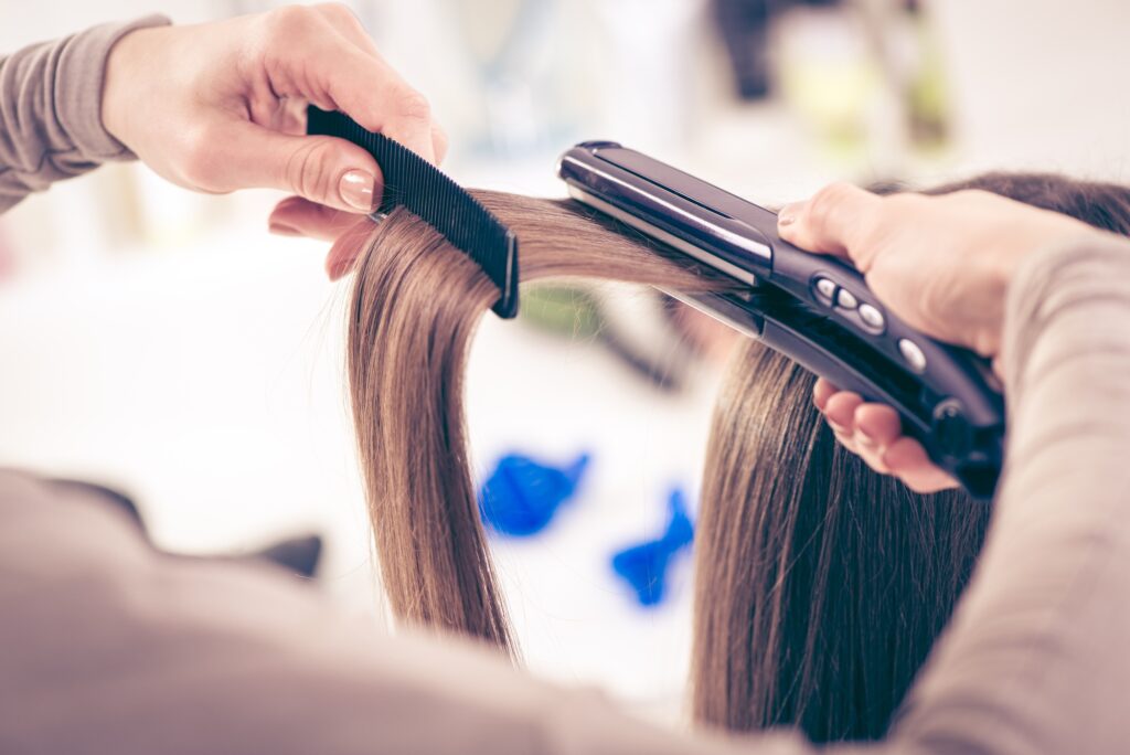 Gros plan d'un coiffeur lissant de longs cheveux bruns avec des fers à cheveux.