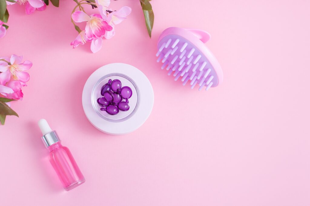 Brosse de shampooing et de massage du cuir chevelu, sérum capillaire et vitamines capillaires sur fond rose, vue de dessus, pose à plat, espace de copie.